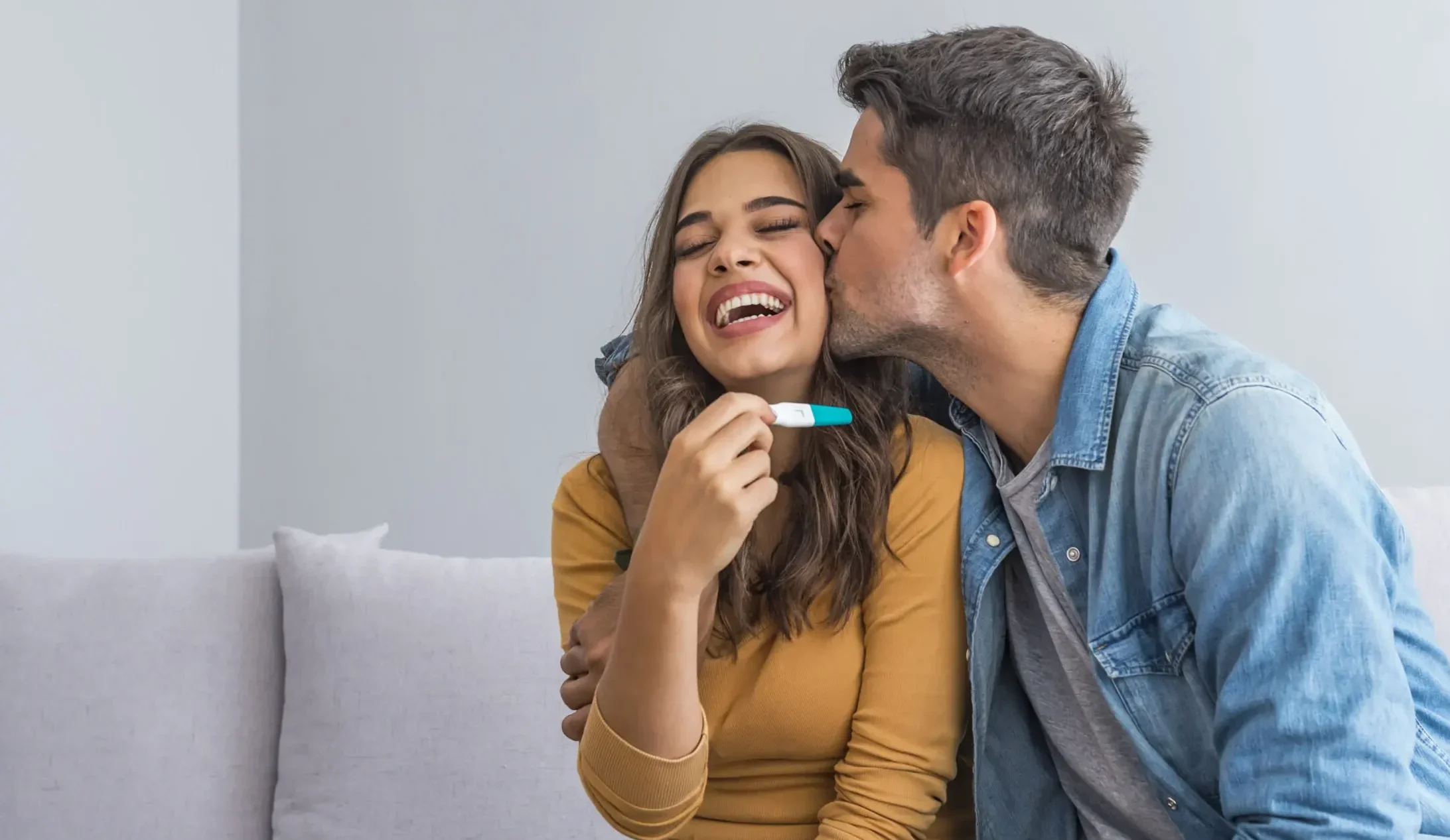 Joyful couple finding out results of a pregnancy test at home. Happy couple looking at pregnancy test. Woman surprising her husband with positive pregnancy test, he seems reasonably pleased