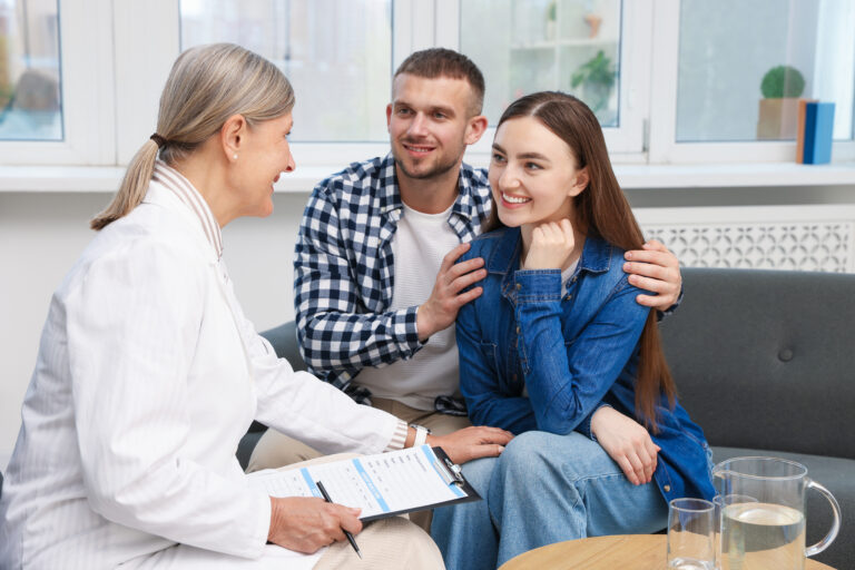 Doctor with a clipboard talking with a smiling couple during a fertility consultation.